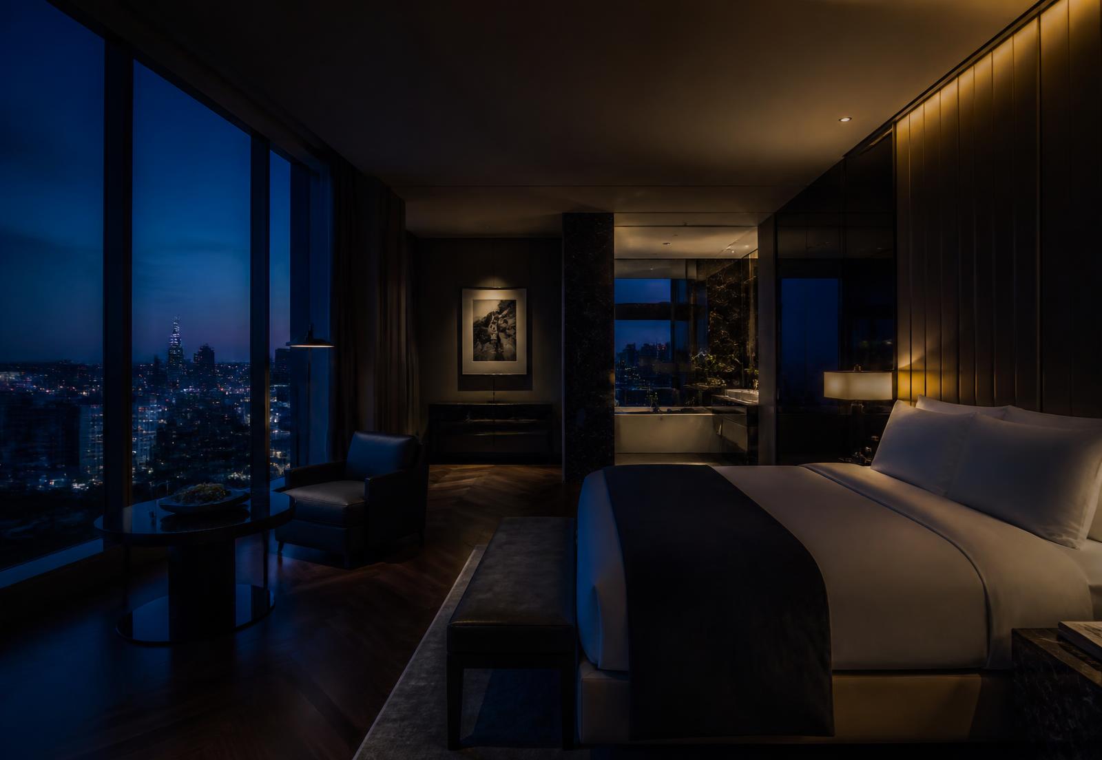 A dark, softly lit luxury hotel suite overlooking a city skyline at dusk